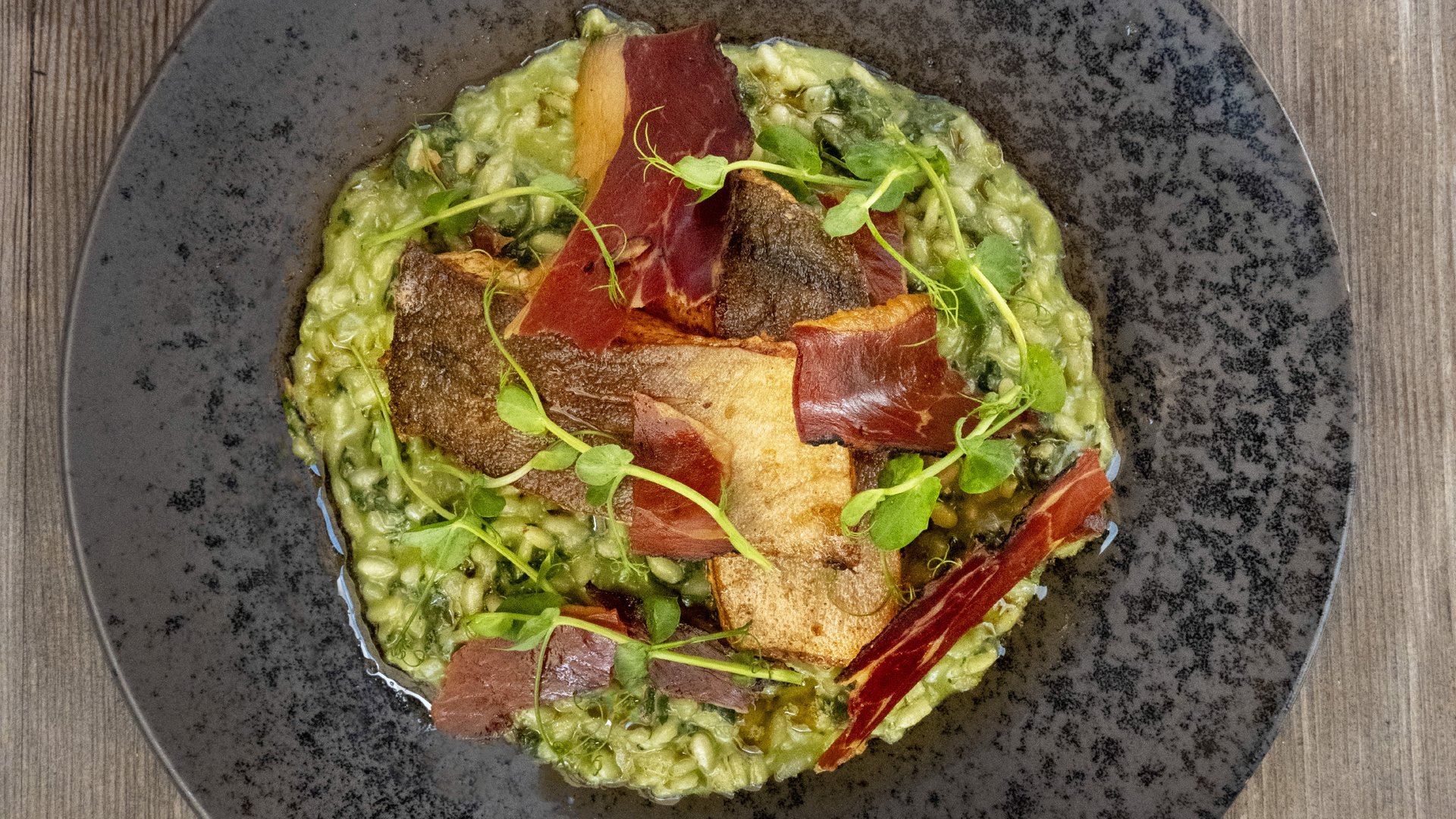Gourmet cuisine from Hotel Bella Vista, creatively presented risotto with crispy duck breast strips on a rustic slate plate.