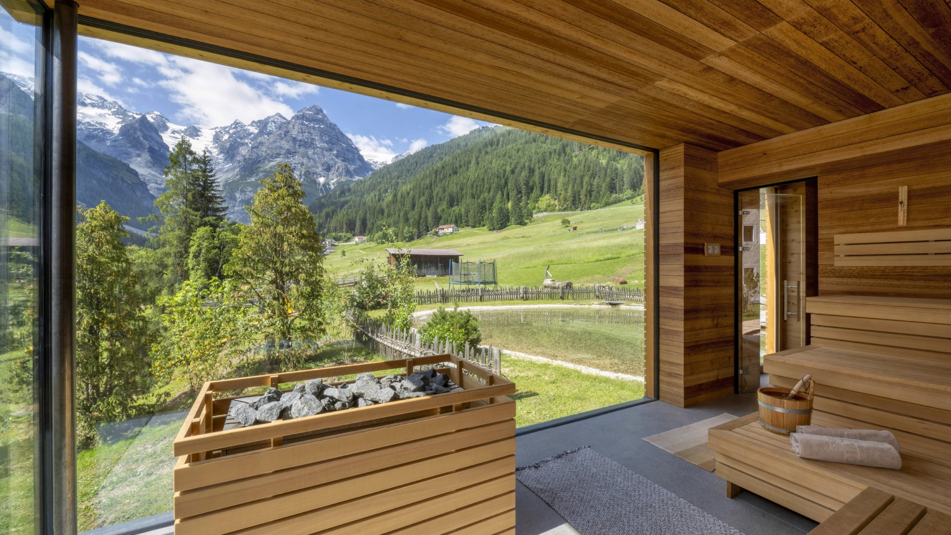 Esperienza estiva di sauna all'Hotel Bella Vista con vista panoramica sul paesaggio alpino verde e sul chiaro panorama del cielo.