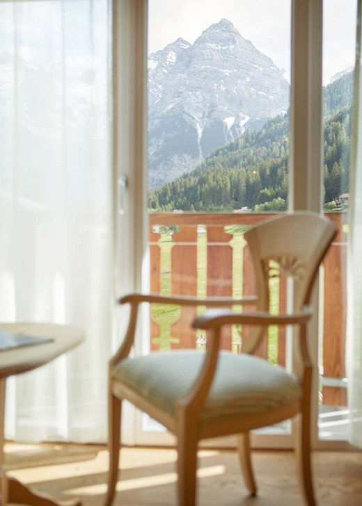 Entspannender Sitzbereich mit Stuhl und Tisch nahe dem Fenster im Hotel Bella Vista, mit inspirierender Aussicht auf die majestätischen Alpen.