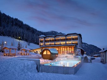 Illuminated Hotel Bella Vista at night, featuring an inviting heated outdoor pool amidst snow-covered mountains and the tranquil winter sky.