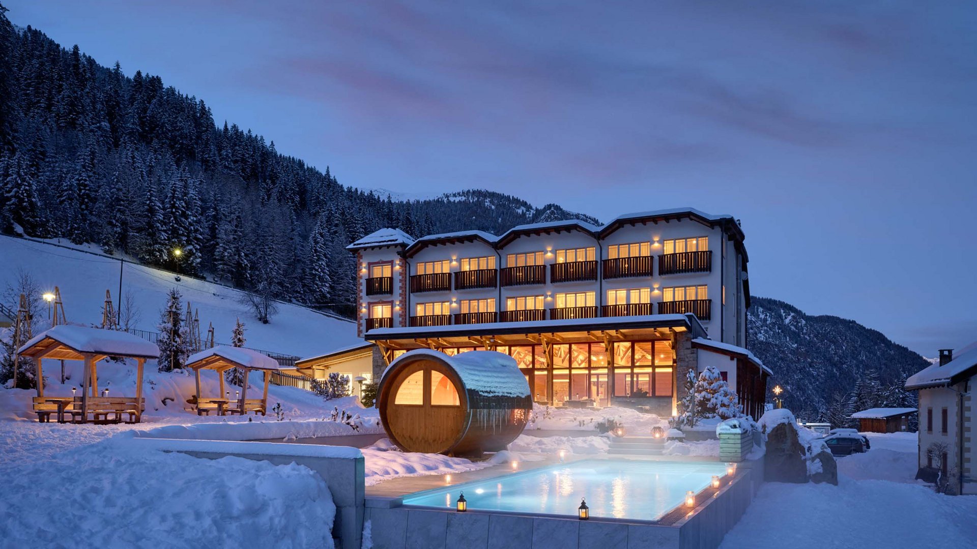 Beleuchtetes Hotel Bella Vista bei Nacht, mit einem einladenden, beheizten Außenpool, umgeben von schneebedeckten Bergen und dem ruhigen Winterhimmel.