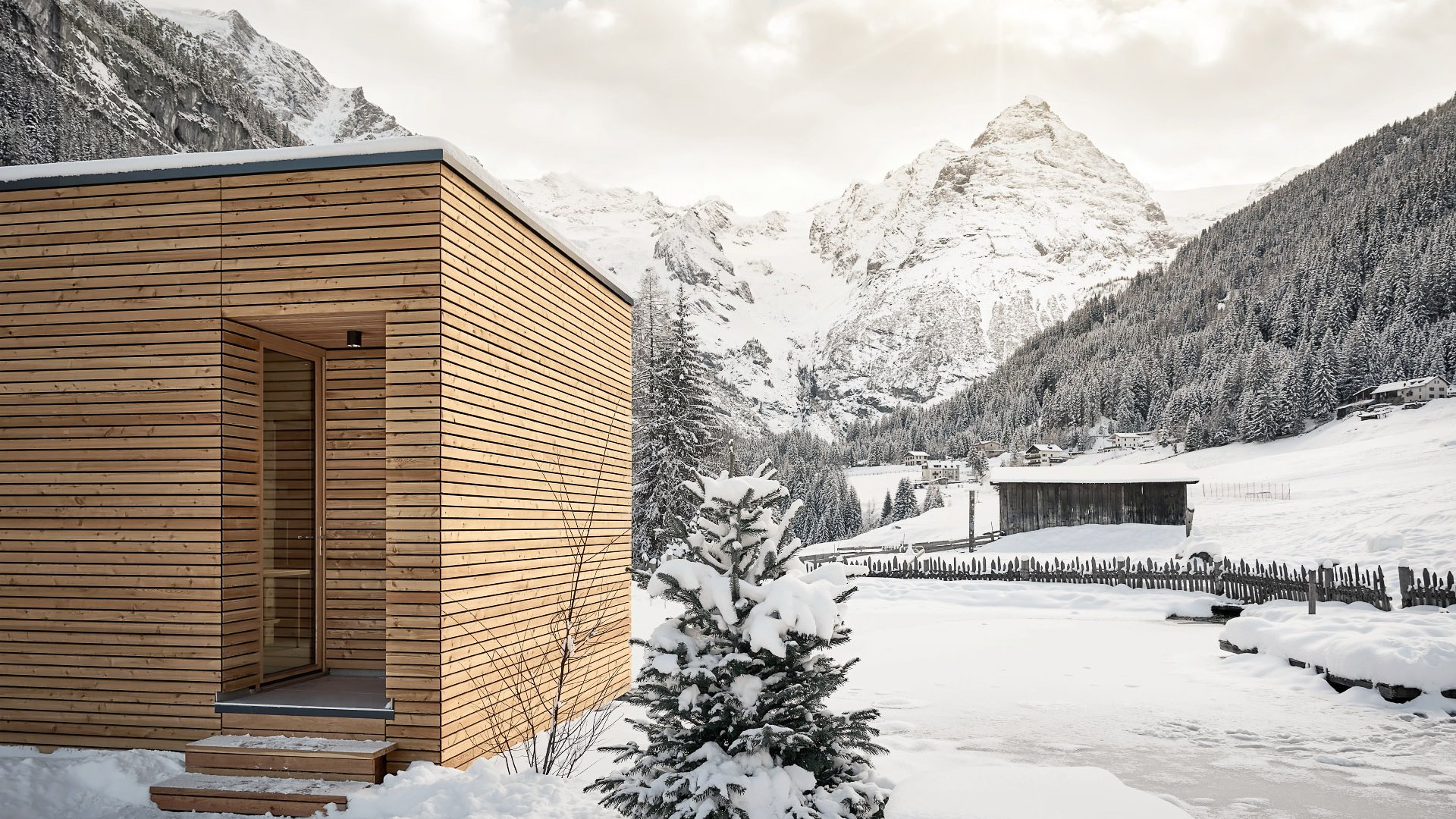 Außensauna mit einzigartiger Holzfassade in einer verschneiten Berglandschaft, Schneeflocken sichtbar im Fall.