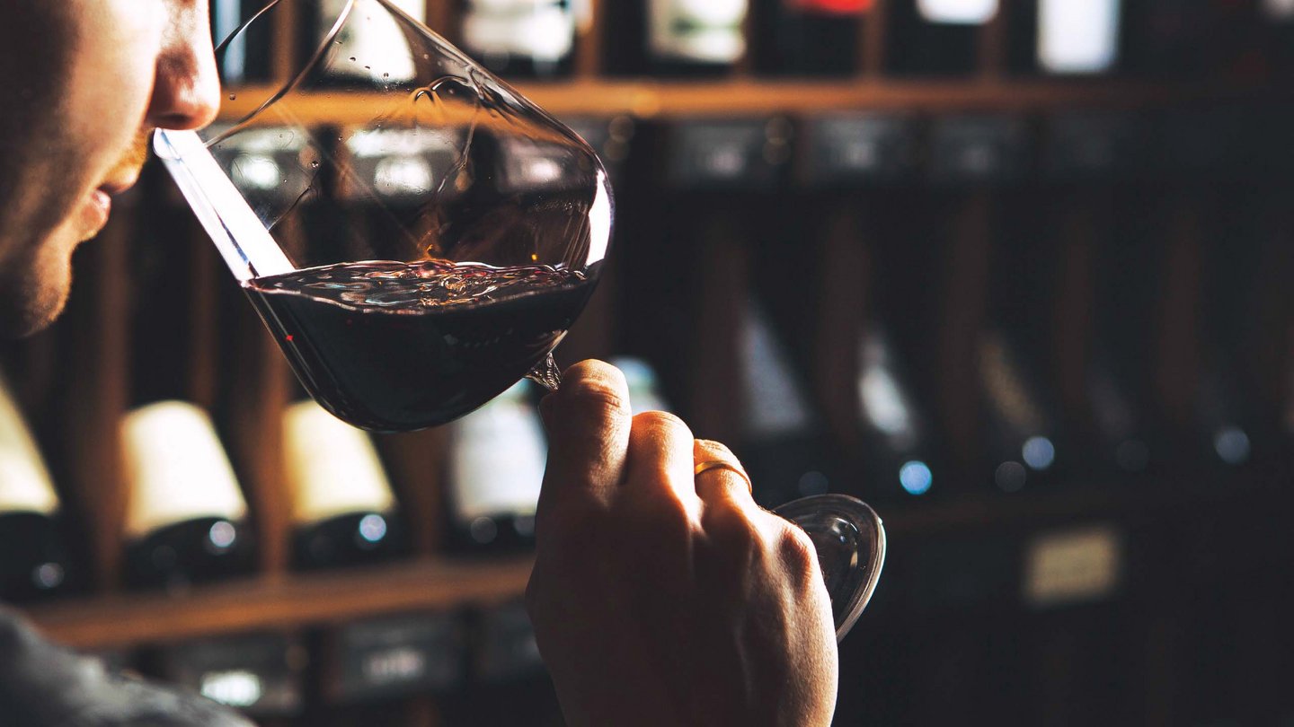 A moment of wine tasting at Hotel Bella Vista, where a guest assesses the quality of a fine red wine against the backdrop of a wine cellar.